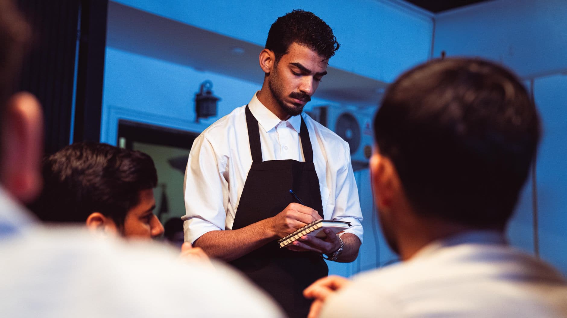 Attentive waiter writing down a customer's order in a cozy indoor restaurant.